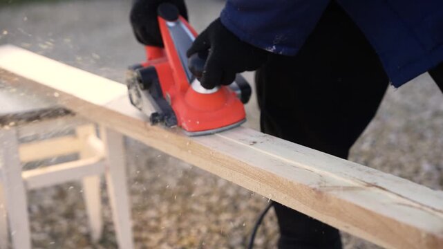 Carpenter planing a wooden board with an electric planer