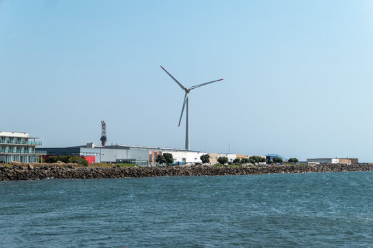 Turbina e&oacute;lica em destaque na zona portu&aacute;ria industrial de Viana do Castelo contra o c&eacute;u azul e flanqueada por edif&iacute;cios industriais no litoral portugu&ecirc;s
