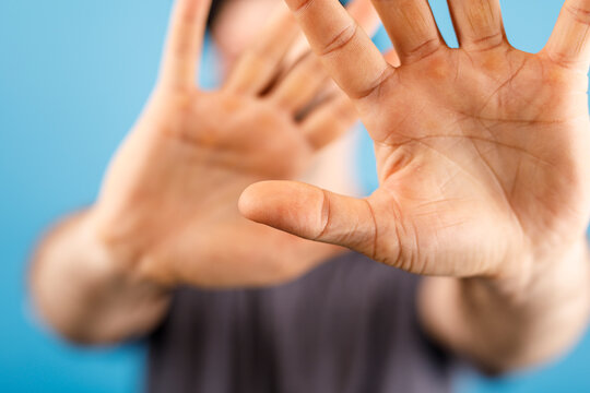 Close-up shot of a person's hands raised in defense, against a light blue background. Illustrating themes of protection, denial, or stop. Perfec