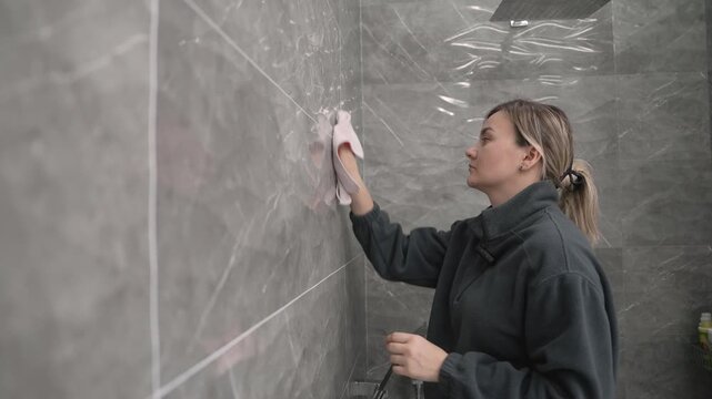 Professional woman cleaning bathroom shower tiled wall