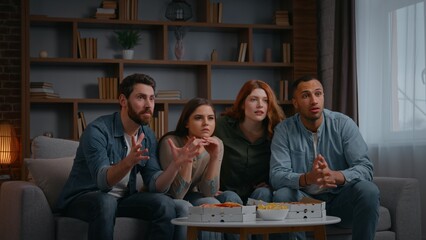 Happy concentrated four multiethnic friends supporting television sport team interested waiting result men women at home party watching tv football fans spectators soccer game on couch sofa together