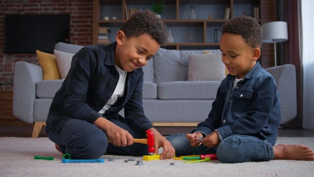 Two ethnic little boys African American kids playing at home joyful play with toys sons siblings children focused with renovation game using repair tools in apartment playful building family indoors - Powered by Adobe