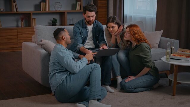 Four multiethnic friends with laptop choosing film online cinema movie at home party discuss order food delivery to domestic event talking looking in computer multiracial diverse men women teamwork