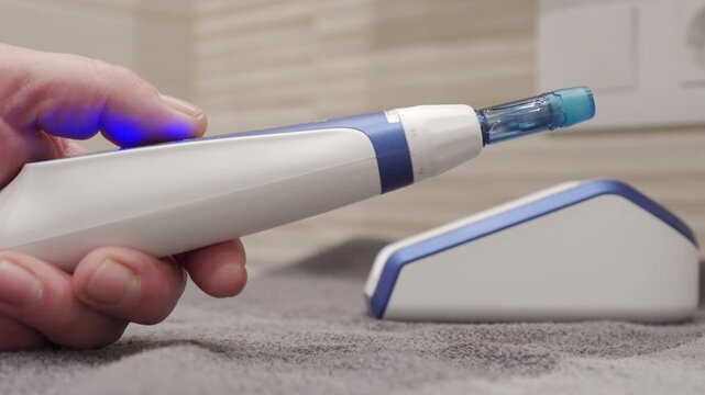 The handheld plastic Dermapen is being operated. It is vibrating for a cosmetic treatment, emitting a continuous buzzing sound.