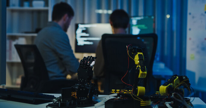 Team adult male engineer collaborate on robotic hand project using AI code solutions machine learning at tech workspace night. Artificial intelligence interface, collaboration prototype development.