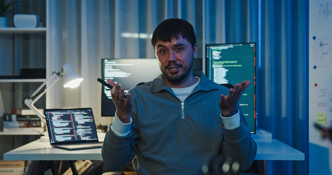 Adult male freelance programmer work late speak in online meeting video conference and looking at camera in tech office night. Artificial intelligence, robotics, user interface, machine learning.