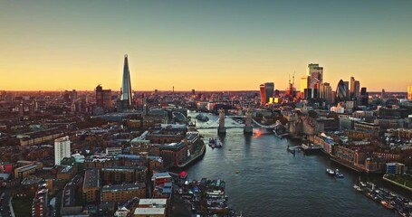 England, aerial London skyline at sunset with iconic landmarks Tower Bridge, The Shard skyscraper, and illuminated buildings of Canary Wharf on River Thames. Modern cityscape under bright evening sky - Powered by Adobe