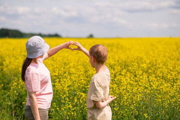 Mother and son making a heart shape with hands while standing in blooming rapeseed field on a sunny day