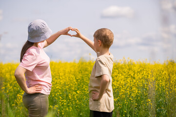 Mother and son making a heart shape with hands while standing in blooming rapeseed field on a sunny day