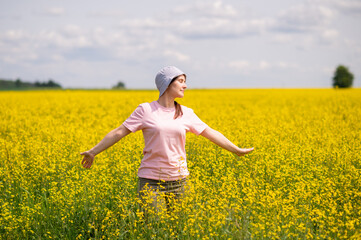 Young woman in bucket hat enjoying a warm summer day in blooming yellow rapeseed field under blue sky