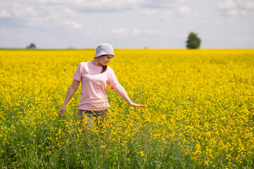 Young woman in bucket hat enjoying a warm summer day in blooming yellow rapeseed field under blue sky