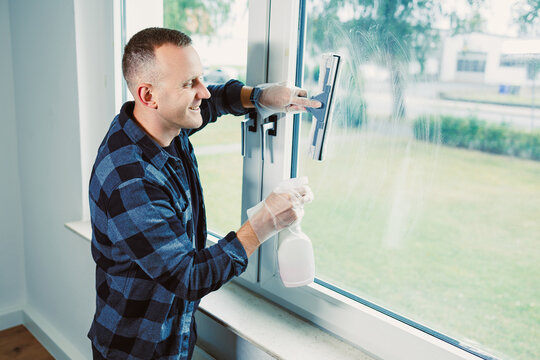 Man cleaning a window in a bright, modern room while enjoying the fresh air and sunshine on a sunny afternoon