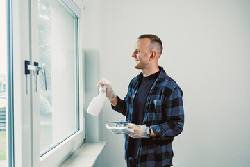 Fototapeta premium Man joyfully cleaning windows in a bright room while preparing for a fresh and tidy living space during a sunny day