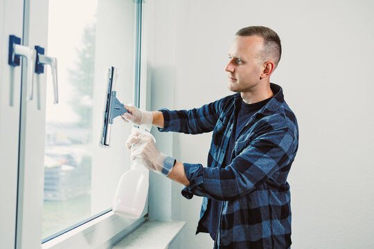 Man cleaning a window with a squeegee in a bright and tidy room during daytime