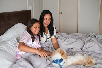 A woman and a girl are laying on a bed with a dog