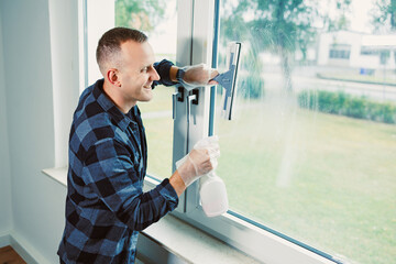 Man cleaning a large window in a modern home during bright daylight while enjoying a refreshing moment of tidiness and clarity