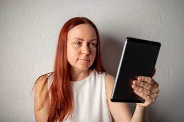 45 year old woman without makeup with long red hair studies tablet device. barefaced natural beauty, clean beauty. Portrait of woman with natural beauty and no makeup, authentic and minimalist look