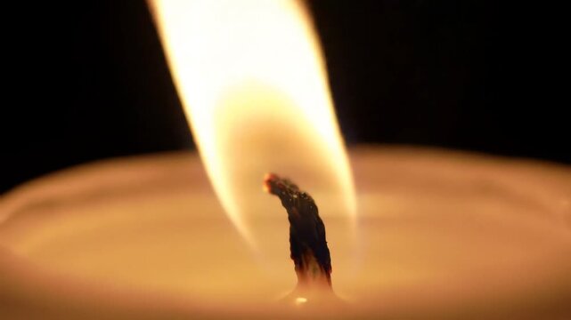 Closeup of a single candle flame burning brightly in the dark casting a warm soft glow and creating a peaceful tranquil atmosphere perfect for meditation or relaxation.
