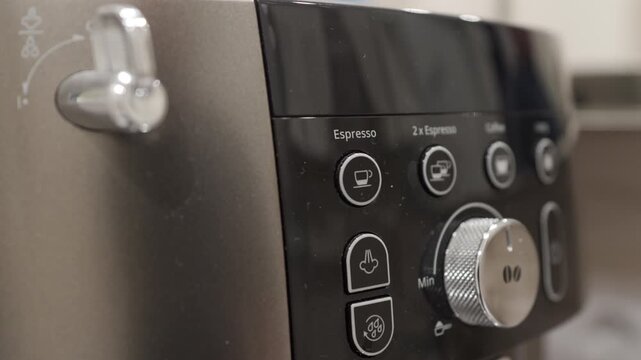 A hand presses the plastic power button on the coffee machine's control panel. The button press triggers a click followed by the internal mechanisms engaging with a whirring and grinding sound.