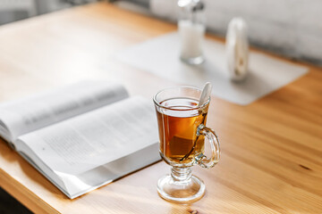 Hot tea in a glass cup beside an open book, cozy reading and relaxing home atmosphere.