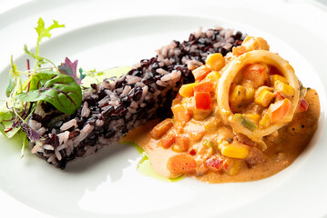 Gourmet seafood dish featuring a stuffed calamari ring in creamy sauce, served alongside black rice and a fresh side salad on a white plate.
