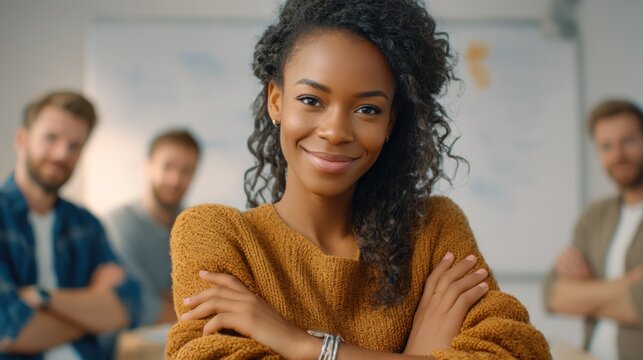 A close-up of a smiling African American woman in a sweater standing in front of her colleagues in an office. Concept of successful business and teamwork.