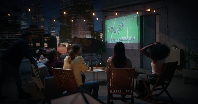 Friends Gather on a Rooftop, Watching Live American Football Match on a Projector. They Enjoy Sports Entertainment, Celebrating Teams Championsip Victory. City View Terrace World Tournament 