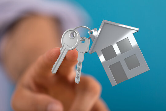Person holding a key with a miniature house keychain symbolizing home ownership, real estate, and the keys to new house. Dream home concept.