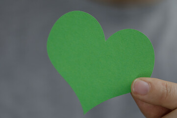 Fototapeta premium A person holding a green paper heart symbol representing love, health, and environmental themes. Perfect for greeting cards, and promoting kind
