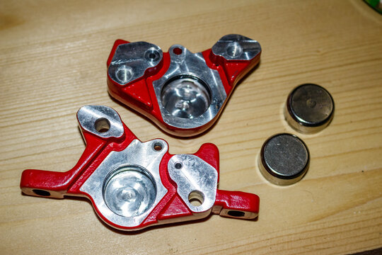 Disassembled red hydraulic bicycle brake calipers, ready for maintenance. Essential MTB cycling components, clean and bright on a wood table