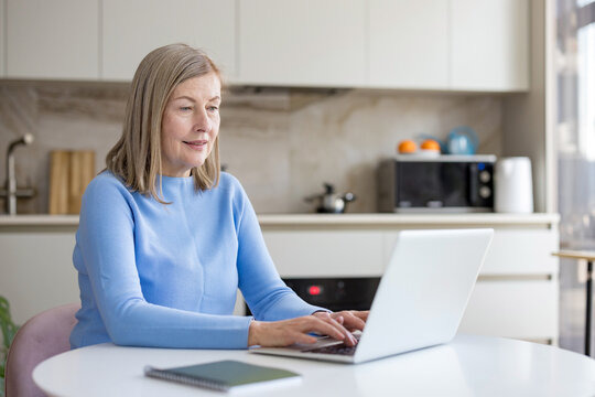 Senior woman focused while typing on a laptop, engaging in remote work or online learning from her modern kitchen table, embracing digital connectivity