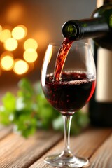 Close-up of red wine being poured into glass with warm golden bokeh in background. Elegant dining, celebration and lifestyle concept