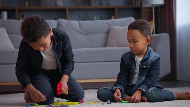 Two African American children playing with plastic toys at home brothers ethnic kids sons boys siblings friends play game repair on floor building with hammer friendship family childhood playtime