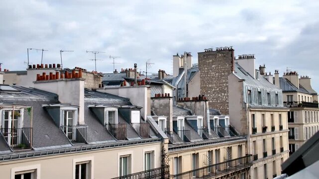 Traditional Haussmann architecture in Paris featuring classic building facades with elegant balconies, zinc mansard roofs, and brick chimneys against a cloudy sky in the capital of France