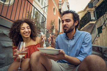 Happy couple eating pasta and drinking wine outdoors in an Italian town