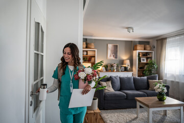 Female nurse arriving home carrying flowers and documents