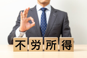 「不労所得」と書かれたブロックとOKポーズをするビジネスマン