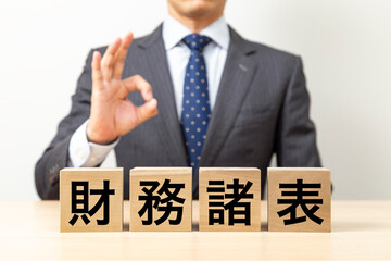 「経常利益」と書かれたブロックとOKポーズをするビジネスマン