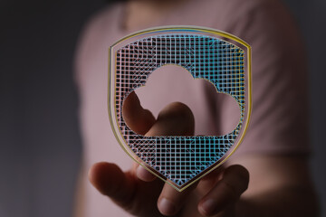 A close-up of a hand holding an illuminated cloud-shaped shield, symbolizing data protection and...