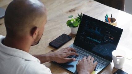 Video of businessman working with statistics on his laptop while using his phone in the office - Powered by Adobe