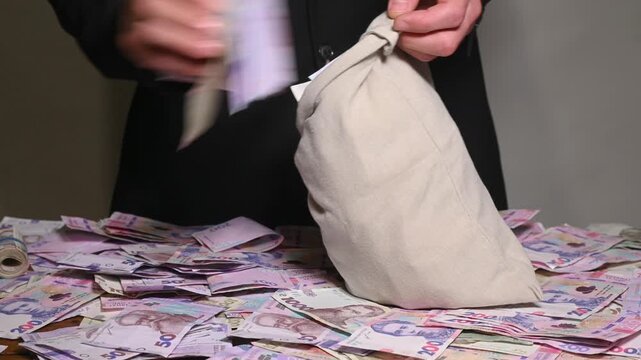 man hurriedly fills bag with stacks of Ukrainian hryvnia, sack full of money representing economic crime and illicit profit. concepts of bribery, theft and hiding illegal cash in Ukraine. - Powered by Adobe