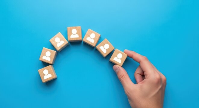 Hand arranging wooden blocks with person icons on blue background - Powered by Adobe