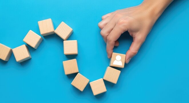 Hand places person icon block into wooden cube sequence on blue.