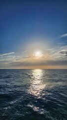 Vertical photo of a glowing sunset over the ocean with sunlight shimmering on the gentle waves. 