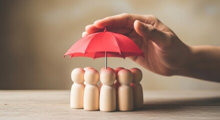 Hand protects wooden figures under a small red umbrella.