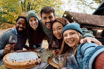 Happy friends taking selfie during Thanksgiving lunch party and looking at camera.