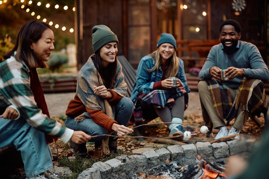 Happy woman and her friends roasting marshmallows on fire in backyard. - Powered by Adobe