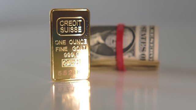 Pure 999.9 gold bullion bar from credit suisse alongside a roll of american dollar currency