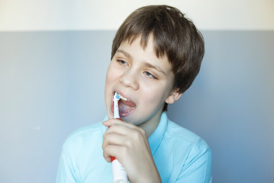 Young boy brushes his teeth with a toothbrush while smiling in a light-colored room in the morning