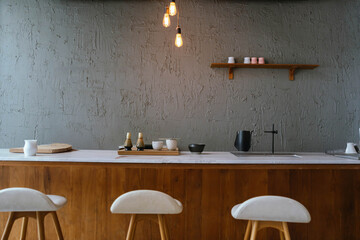 Modern minimalist kitchen interior with wooden counter, bar stools, warm lighting, and simple decor creating a cozy and stylish atmosphere.